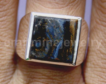 May include: A silver ring with a square, blue gemstone with gold and black veining. The ring is set in a polished silver band. The gemstone is the focal point, showcasing a natural pattern.