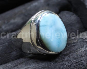 Könnte beinhalten: Ein silberner Ring mit einem großen, ovalen, hellblauen Edelstein. Der Edelstein hat ein marmoriertes Aussehen mit weißen und grünen Farbtönen. Der Ring liegt auf einer dunklen, strukturierten Oberfläche.