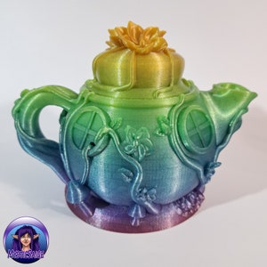 May include: A rainbow iridescent teapot with a flower on top and vines and windows on the sides. The teapot is made of a smooth, shiny material.