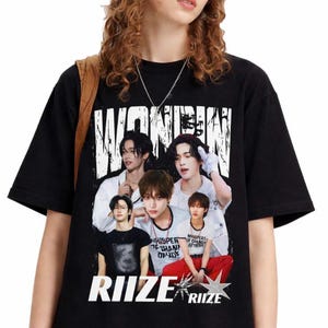 May include: Black t-shirt featuring a graphic of a musical group with the word "WONBIN" in large white letters at the top. The word "RIIZE" is printed at the bottom in white, with a star graphic.