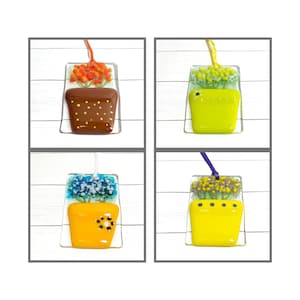 May include: Four glass flower pot ornaments with different colored flowers and pots. The pots are brown, green, yellow, and yellow. The flowers are orange, white, blue, and yellow.