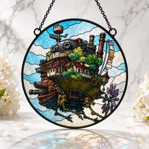 May include: A circular stained glass suncatcher featuring a detailed depiction of a complex, multi-tiered mechanical castle with brown, green, and red elements, suspended by a black metal chain against a light blue and white cloudy sky background.