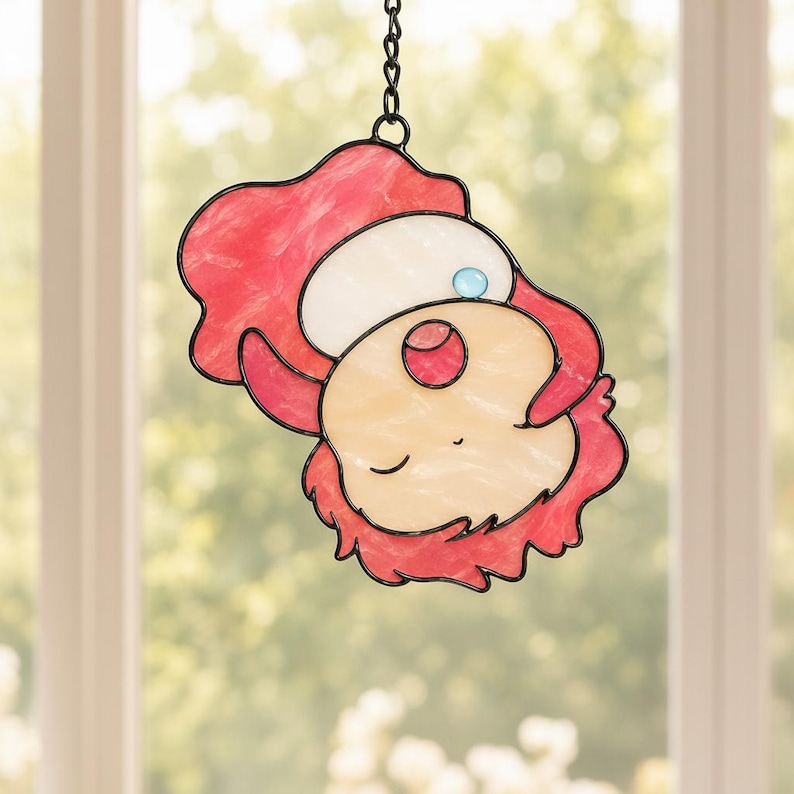 May include: A stained glass window decoration featuring a cartoon character with a red and white hat, red hair, and a light yellow face. The character has a blue gem on the hat and is outlined in black. The window hangs from a chain.