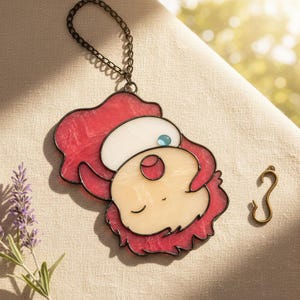 May include: A stained glass pendant featuring a cartoon character with red hair, a white hat, and a light skin tone. The pendant has a black outline and a small blue gem. A bronze-colored chain and hook are also visible.