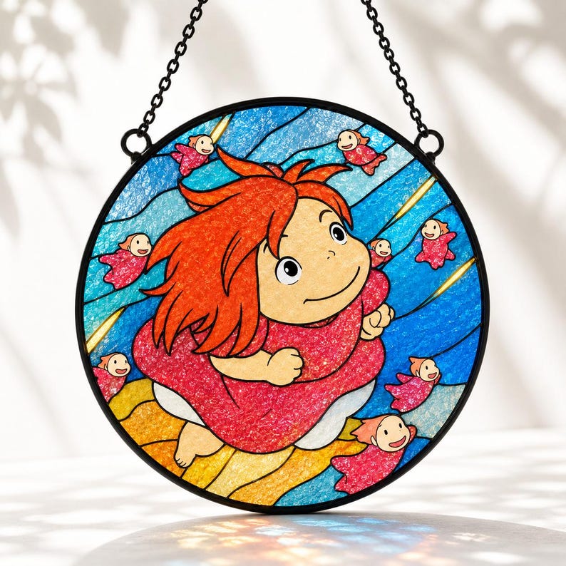 May include: A circular stained glass suncatcher featuring a central character with bright orange hair and a pink dress, surrounded by small pink fish-like figures against a blue wavy background. The piece is framed in black and hangs by a metal chain.
