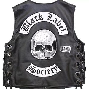 Puede incluir: Chaleco de cuero negro con un gráfico de calavera y las palabras "Black Label Society" y "Society" en parches blancos. El chaleco tiene laterales con cordones y cierre de botón en la parte inferior.