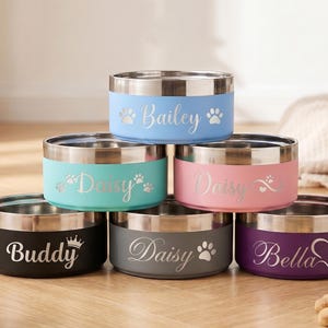 May include: A stack of six stainless steel pet bowls with colored exteriors. Each bowl has a silver rim and is personalized with a pet's name and paw print or heart design. Colors include blue, teal, pink, black, gray, and purple.