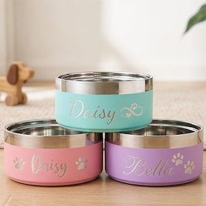 May include: Three stainless steel pet bowls in pastel colors: light blue, pink, and purple. Each bowl has a silver rim and is personalized with a pet's name in cursive script. Paw prints and hearts are also featured.