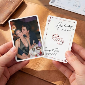 Könnte beinhalten: Zwei Spielkarten werden in Händen gehalten. Eine Karte zeigt ein Foto eines Paares, die andere Karte trägt den Text "How lucky are we?" und Würfelillustrationen. Die Karte enthält auch die Namen "Tenny & Tony" und das Datum "02.14.26".