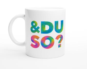 Può includere: Tazza in ceramica bianca con la scritta "& DU SO?" in lettere colorate e vorticose. La tazza ha un manico curvo e un design semplice, adatta per bevande calde.