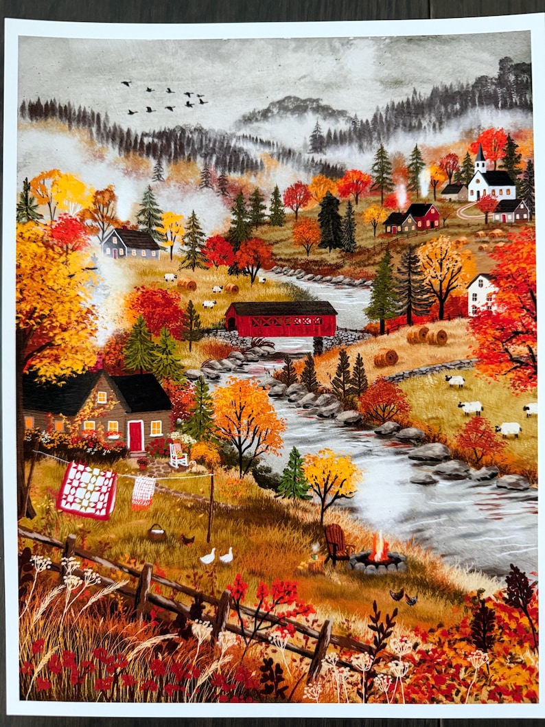 May include: A painting of an autumn landscape featuring a river flowing through a valley with a red covered bridge, houses, a church, and sheep. A clothesline with a quilt, a campfire, and trees with orange and yellow foliage are visible.