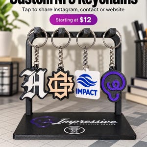 Pode incluir: Quatro porta-chaves NFC personalizados pendurados num suporte preto. Os porta-chaves apresentam vários designs, incluindo uma letra H branca, um logótipo geométrico bege, um quadrado branco com uma onda azul e o texto IMPACT, e um ícone circular roxo.