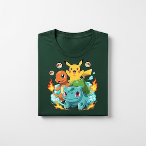 Peut inclure: T-shirt vert fonc&eacute; avec un motif de Pikachu, Salam&egrave;che et Bulbizarre. Les personnages de dessins anim&eacute;s sont entour&eacute;s de flammes et de nuages. Le t-shirt est pli&eacute;.