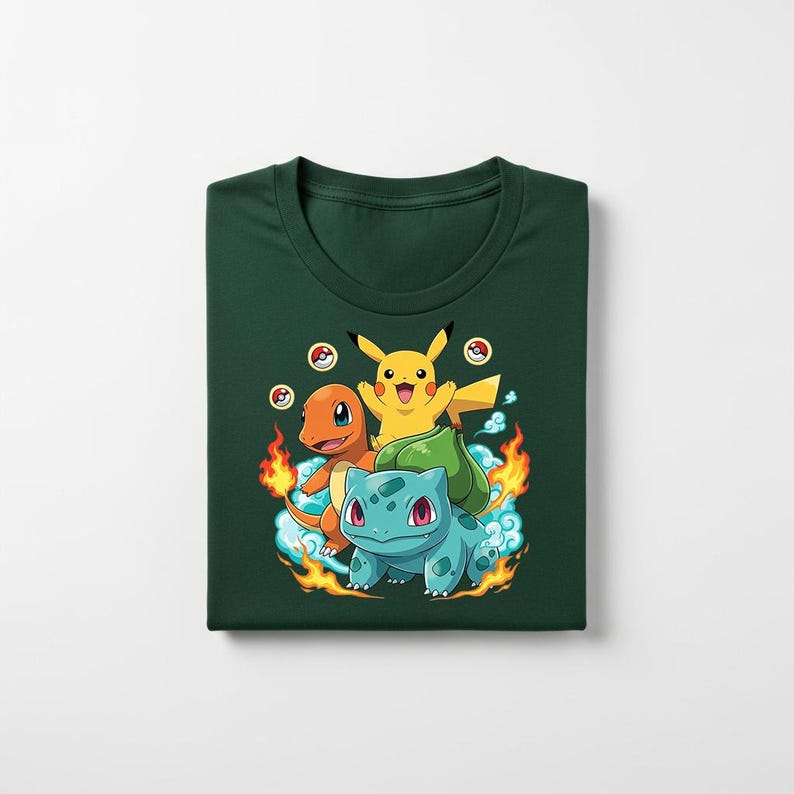Peut inclure: T-shirt vert fonc&eacute; avec un motif de Pikachu, Salam&egrave;che et Bulbizarre. Les personnages de dessins anim&eacute;s sont entour&eacute;s de flammes et de nuages. Le t-shirt est pli&eacute;.