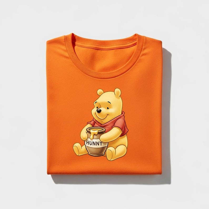 May include: An orange t-shirt featuring a cartoon illustration of Winnie the Pooh holding a honey pot. The honey pot is brown with the word "HUNNY" printed on it. Winnie the Pooh is wearing a red shirt.