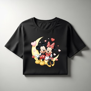 May include: Black t-shirt featuring Mickey and Minnie Mouse sitting on a crescent moon. The cartoon couple is surrounded by pink hearts. Mickey wears red shorts, and Minnie wears a red dress with a polka dot bow.