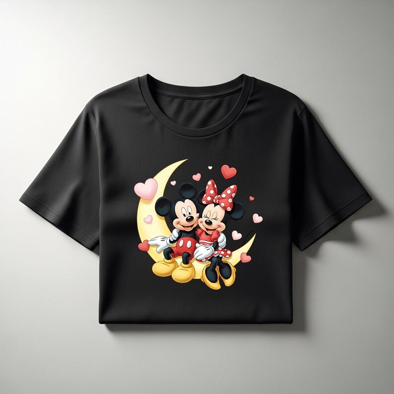 May include: Black t-shirt featuring Mickey and Minnie Mouse sitting on a crescent moon. The cartoon couple is surrounded by pink hearts. Mickey wears red shorts, and Minnie wears a red dress with a polka dot bow.