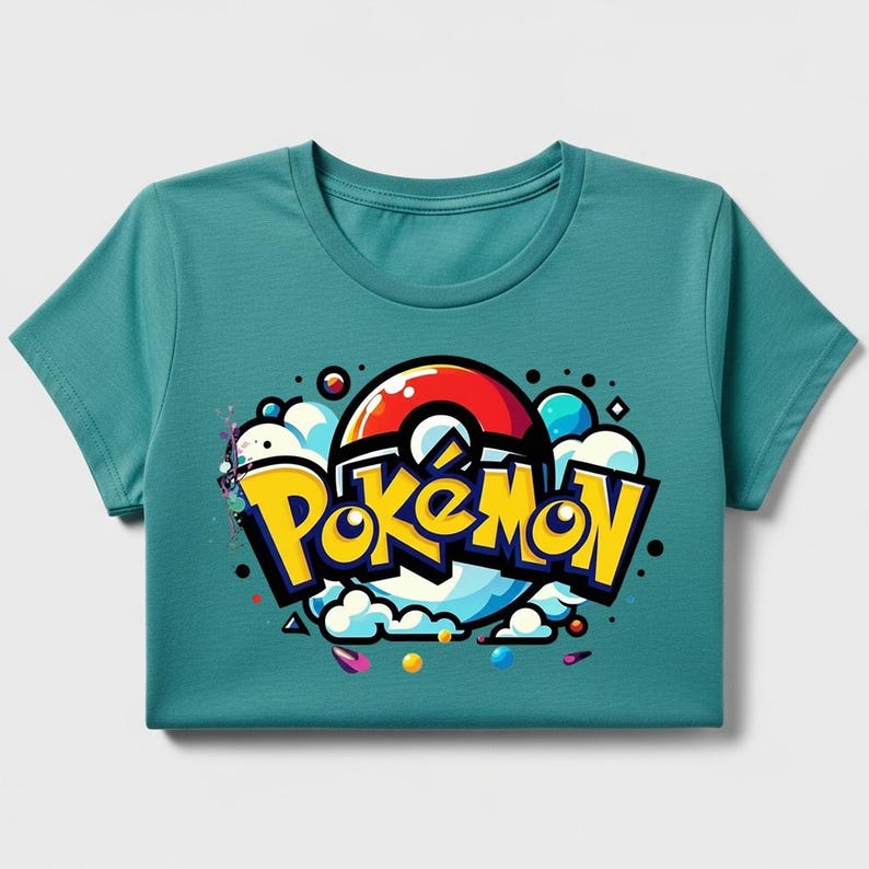 Peut inclure: T-shirt turquoise avec le mot "Pok&eacute;mon" en jaune, soulign&eacute; de noir, et un design de Pok&eacute; Ball rouge et blanc. Le graphisme comprend des nuages blancs, des accents bleus et jaunes et des points color&eacute;s.