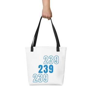 May include: White tote bag with black handles, held by a person. The bag features the number "239" in blue, repeated three times. The bag is made of a sturdy material and is suitable for carrying various items.