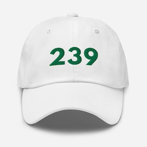 May include: White baseball cap with the number "239" embroidered in green on the front. The cap has a curved brim and a classic six-panel design. A casual accessory for everyday wear.