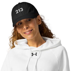 Può includere: Cappellino da baseball nero con il numero "213" in bianco. Il cappellino è indossato da una persona che indossa una felpa con cappuccio bianca.