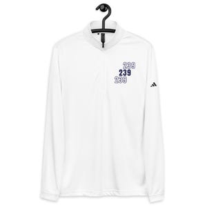 Puede incluir: Camiseta deportiva blanca de manga larga con cuello con cremallera. La camiseta presenta el número "239" apilado tres veces en azul marino, con el logo de Adidas en la manga. Cuelga de una percha negra.