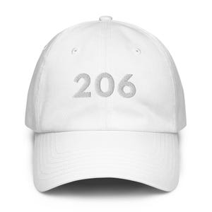 Peut inclure: Casquette de baseball blanche avec une visière incurvée. Le chiffre "206" est brodé en fil gris clair sur le devant. La casquette a un design classique à six panneaux et une sangle réglable à l'arrière.