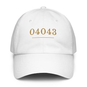 Op de afbeelding: Witte baseballpet met een gebogen klep. De pet heeft het geborduurde nummer "04043" in goud, met een gouden lijn eronder. De pet is gemaakt van een zacht materiaal en heeft een klassieke, casual stijl.