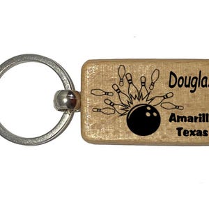 May include: A wooden keychain with a silver key ring. The keychain features a bowling ball and pins graphic with the text "Douglas Amarillo Texas".