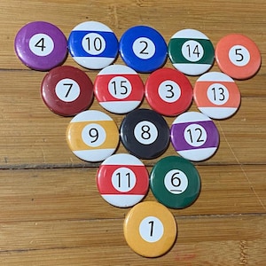May include: A set of 15 round, colorful, numbered billiard ball pins. The pins are arranged in a triangle shape on a wooden surface. The numbers on the pins range from 1 to 15.