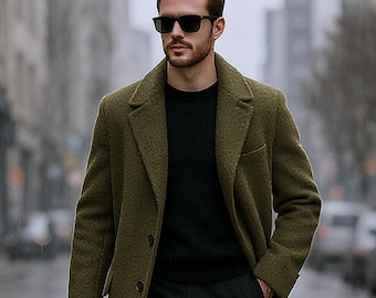 May include: An olive green wool overcoat worn over a black sweater and dark trousers. The outfit includes black leather boots, black sunglasses, and a closed black umbrella held in one hand. The coat features a notched lapel and two front buttons.