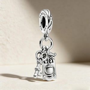 Könnte beinhalten: Ein silberner Charm-Anhänger mit einem Schlüssel und einer Tür mit Gesicht, verbunden durch einen Ring mit einem Pandora-Markenbügel. Der Charm besteht aus poliertem Metall und hat aufwendige Details.