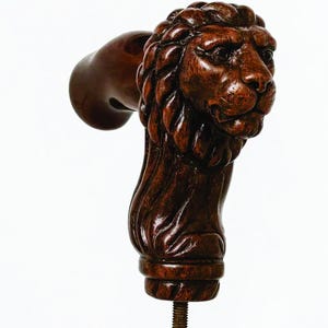 Puede incluir: Escultura detallada de madera marrón oscuro con cabeza de león, probablemente un tirador de mueble o elemento decorativo. La melena y los rasgos faciales del león están intrincadamente tallados, con un perno roscado que se extiende desde la base.