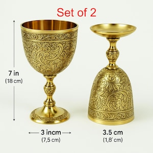 Pode incluir: Um conjunto de 2 cálices de metal dourado com padrões florais em relevo. O cálice mais alto mede 18 cm de altura com um diâmetro de 7,5 cm. O conjunto inclui um design correspondente para a base e a haste de cada peça.