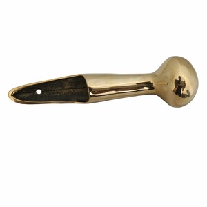 Puede incluir: Un tirador de puerta de lat&oacute;n pulido con un extremo redondeado y una abertura rectangular. El tirador es de color dorado c&aacute;lido y parece estar hecho de metal. El tirador est&aacute; dise&ntilde;ado para montarse en una puerta.