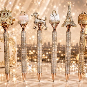 May include: A set of six rose gold pens with barrels covered in clear crystals. Each pen features a unique topper: a carriage, a pink stone, a poodle, a white stone, the Eiffel Tower, and a tan stone. All toppers are accented with crystals.