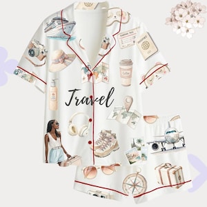 以下が含まれることがあります： 旅行をテーマにしたプリントの白いパジャマセット。半袖トップスとショートパンツには、クルーズ船、カメラ、パスポート、地図、そして「Travel」の文字のイラストが描かれています。赤いトリムが縁を飾っています。