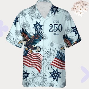 Puede incluir: Camisa azul claro de manga corta con un diseño patriótico. Presenta una bandera estadounidense, águilas, fuegos artificiales y estrellas. La camisa tiene los números "1776", "250" y "2026" impresos. Una camisa casual.