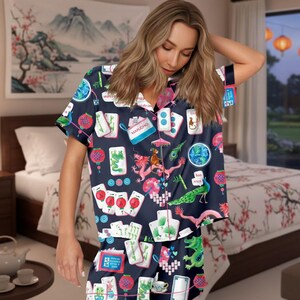 May include: Navy blue pajama set featuring a Mahjong tile print with dragons, lanterns, and other game-related graphics. The set includes a short-sleeved button-up shirt and matching shorts. The shirt has pink trim.