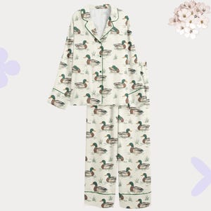 May include: Cream-colored pajama set featuring a repeating pattern of ducks on a pond. The long-sleeved top and pants have green trim. The pajamas are made of a soft, lightweight fabric.