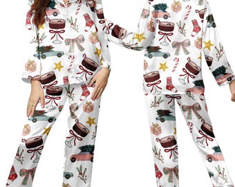 May include: White satin pajama set with a festive Christmas pattern. The print includes images of cars with Christmas trees, gift boxes, bows, stars, candy canes, and socks. The long-sleeved top has a button-down front and the pants have an elastic waistband.