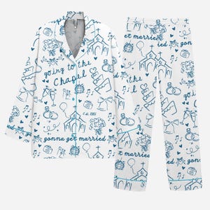 May include: White pyjama set with a blue wedding-themed design. The set features a button-down shirt and trousers, both decorated with illustrations of churches, wedding rings, cakes, and the phrases "going to the chapel" and "gonna get married".