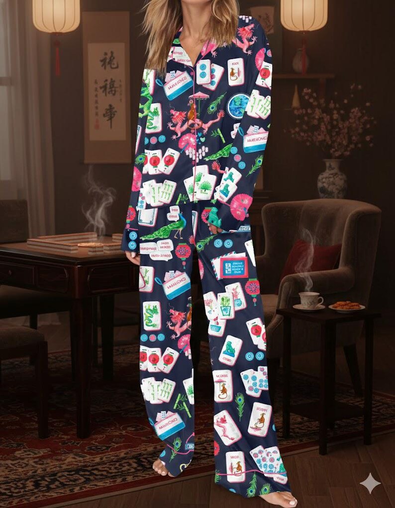 May include: Navy blue pajama set with a colorful print of Mahjong tiles, dragons, and peacocks. The long-sleeved top has a button-down front and a pink floral collar. The matching pants have a relaxed fit. The set is made of a soft, comfortable material.