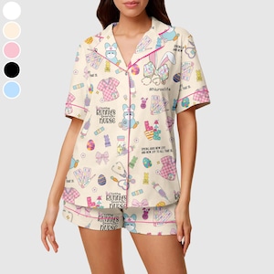 May include: A two-piece pajama set featuring a cream-colored top and shorts. The set is adorned with a repeating pattern of Easter-themed medical illustrations, bunnies, and the text "Every bunny's favorite nurse." The trim is pink.