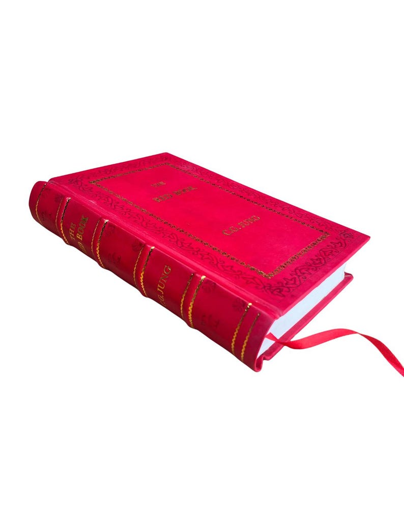 Op de afbeelding: Een rood hardcover boek met gouden letters en een bijpassend rood lint als bladwijzer. De kaft van het boek toont de titel en de naam van de auteur in goud. De rug heeft gouden banden en de naam van de auteur.