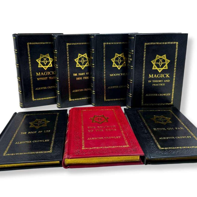 K&ouml;nnte beinhalten: Eine Sammlung von Hardcover-B&uuml;chern mit goldfarbenen Buchstaben und Designs. Die B&uuml;cher sind schwarz, mit einem roten Buch in der Mitte. Zu den Titeln geh&ouml;ren "Magick", "The Book of Lies" und "Konx Om Pax" von Aleister Crowley.