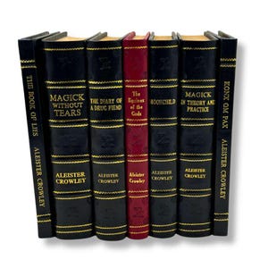 K&ouml;nnte beinhalten: Eine Sammlung von Hardcover-B&uuml;chern, darunter "Magick Without Tears" und "The Book of Lies" von Aleister Crowley. Die B&uuml;cher sind schwarz mit goldenen Buchstaben und Akzenten, mit Ausnahme eines roten Buches.