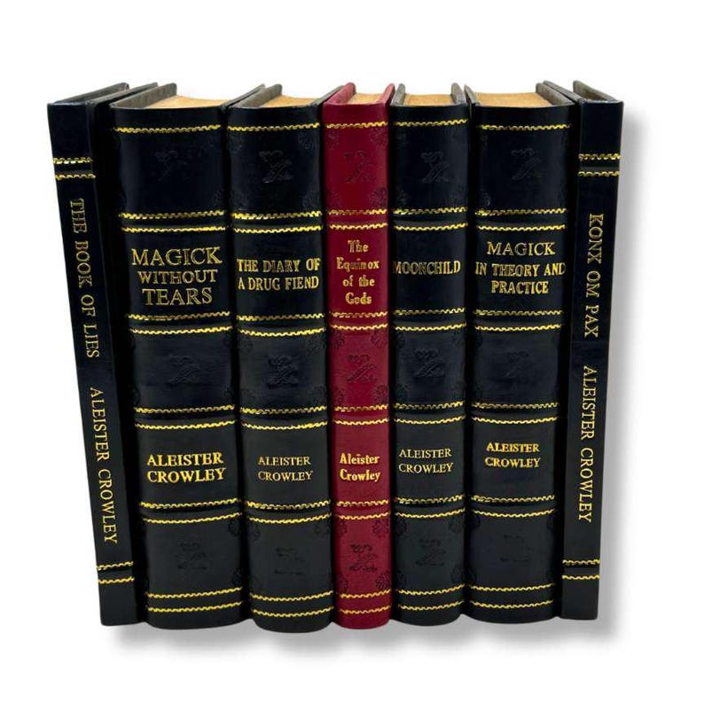 K&ouml;nnte beinhalten: Eine Sammlung von Hardcover-B&uuml;chern, darunter "Magick Without Tears" und "The Book of Lies" von Aleister Crowley. Die B&uuml;cher sind schwarz mit goldenen Buchstaben und Akzenten, mit Ausnahme eines roten Buches.