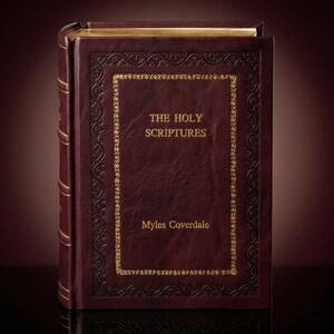 May include: A maroon leather-bound book with gold detailing. The cover displays the title "THE HOLY SCRIPTURES" and the author's name, "Myles Coverdale," in gold. The book has a decorative gold border and a reflective surface.