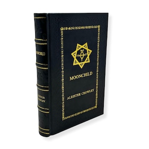 May include: A black hardcover book titled "MOONCHILD" by Aleister Crowley. The cover features gold lettering and a gold star-like emblem. The spine also has gold lettering. The book is presented against a white backdrop.